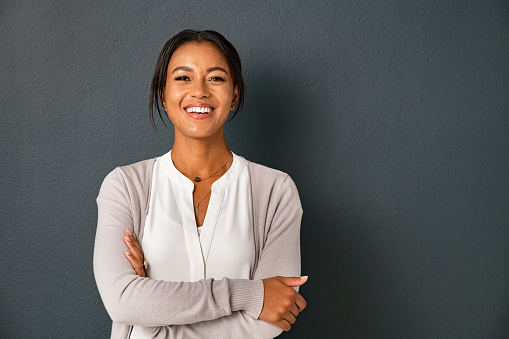 Sponsored image (1) Beautiful mid adult african american woman standing on grey wall with crossed arms. Mature indian woman isolated on gray background. Portrait of smiling hispanic lady looking at camera with satisfaction.